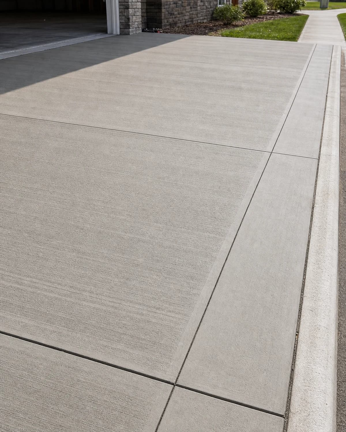 Broom-finished concrete driveway edge with clean expansion joint, apron transition, and realistic concrete texture