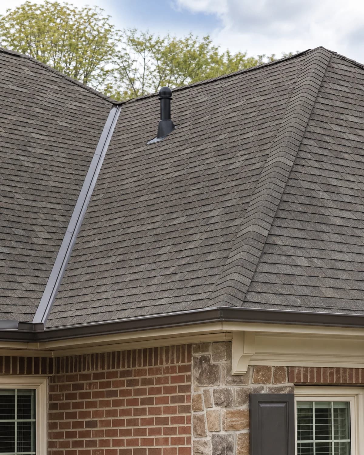 Finished residential roof detail with asphalt shingles, flashing, vent, and clean alignment